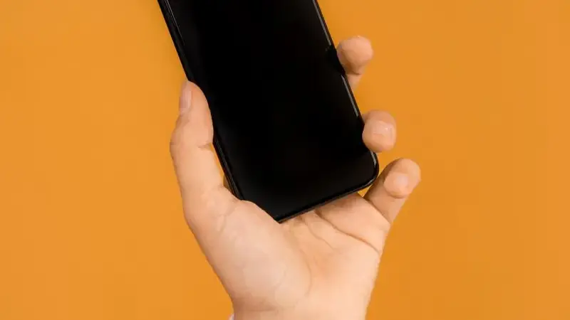 Hand holding a smartphone against an orange background for the update guide